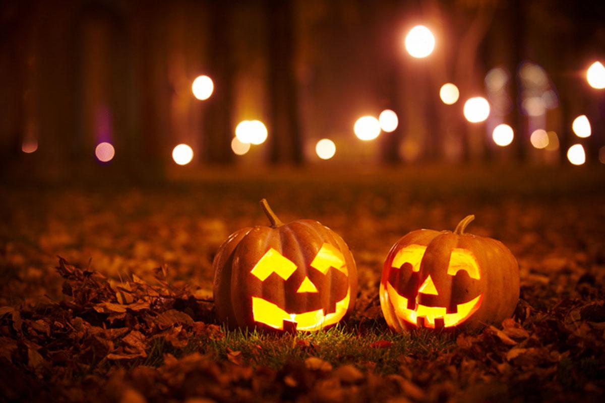 Two jack-o-lanterns with lights shining through the trees in the background.